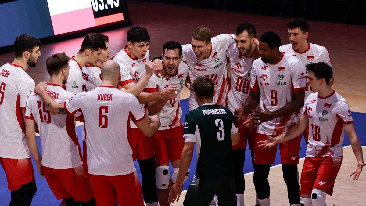 Grupa siatkarzy w białych strojach z czerwonymi numerami świętuje zwycięstwo, obejmując się ramionami. W centrum stoi zawodnik w zielonym stroju.