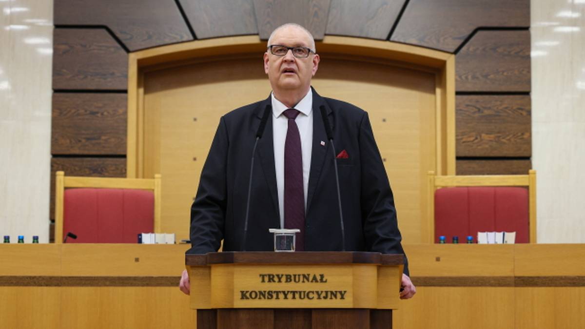 Mężczyzna w garniturze i krawacie stoi za m&oacute;wnicą z napisem "Trybunał Konstytucyjny".