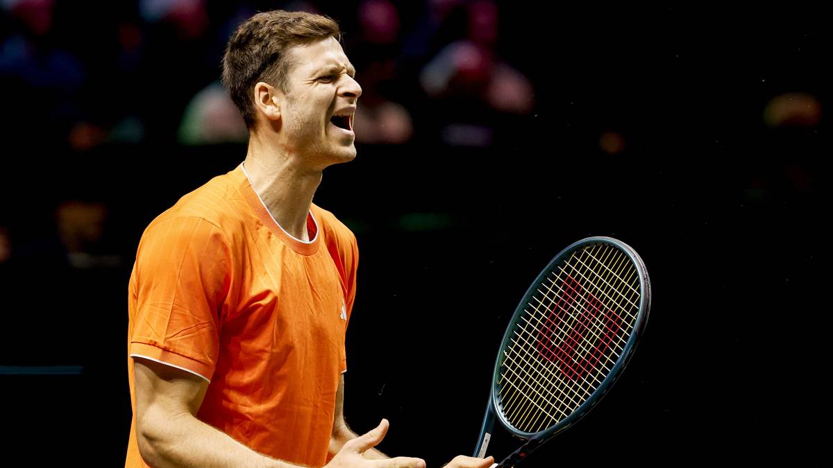 Tenisista w pomarańczowej koszulce krzyczy podczas meczu, trzymając rakietę tenisową.