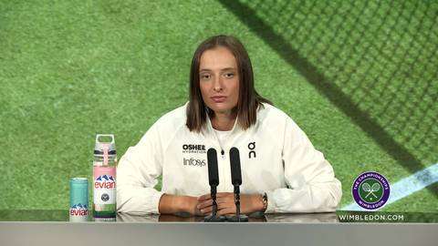 Iga Świątek siedzi przy stole konferencyjnym, za nią zielone tło imitujące trawę tenisową.