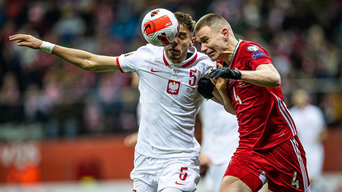 Piłkarz w białej koszulce reprezentacji Polski walczy o piłkę z zawodnikiem w czerwonej koszulce.