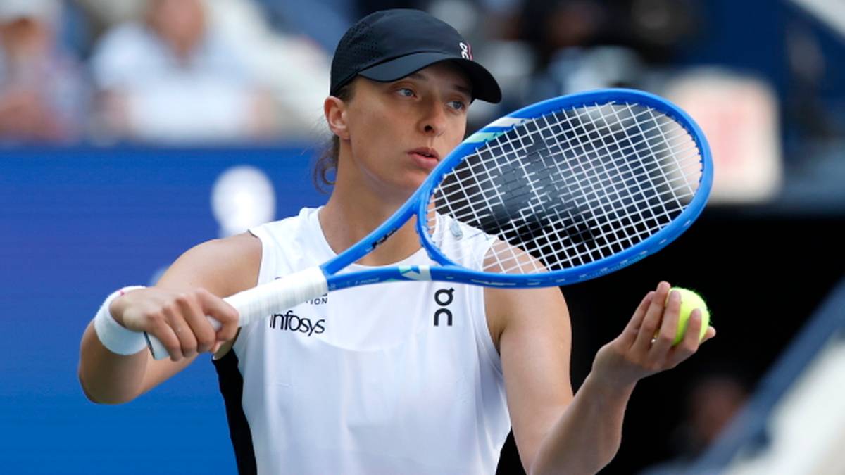 Iga Świątek podczas meczu tenisa, trzymająca rakietę i piłkę.