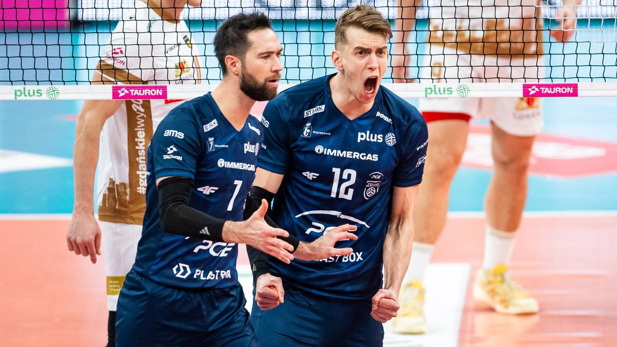 Dwóch siatkarzy w granatowych koszulkach z numerami 7 i 12, w trakcie meczu, jeden z nich pokazuje emocje w kierunku widza, wyrażając reakcję sportową.