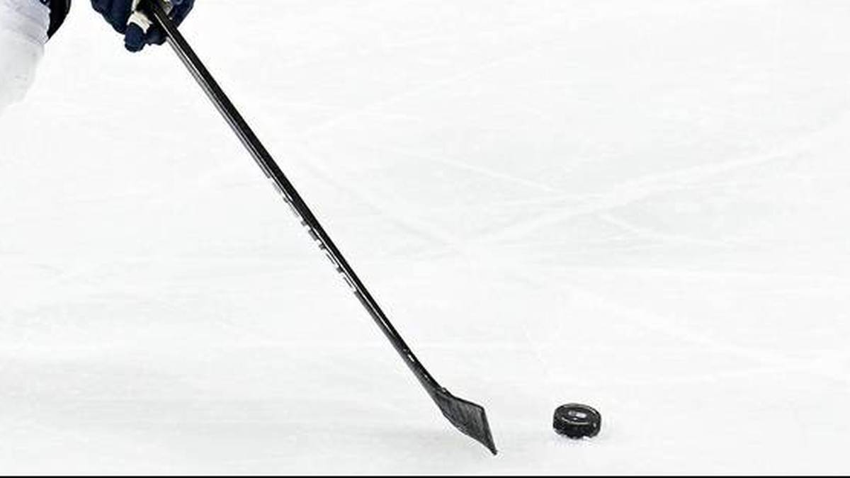 Dłoń w rękawicy hokejowej trzyma kij nad krążkiem na lodowisku.