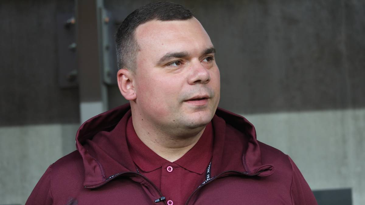 Portret mężczyzny w bordowej bluzie z kapturem, zwracającego się w bok.