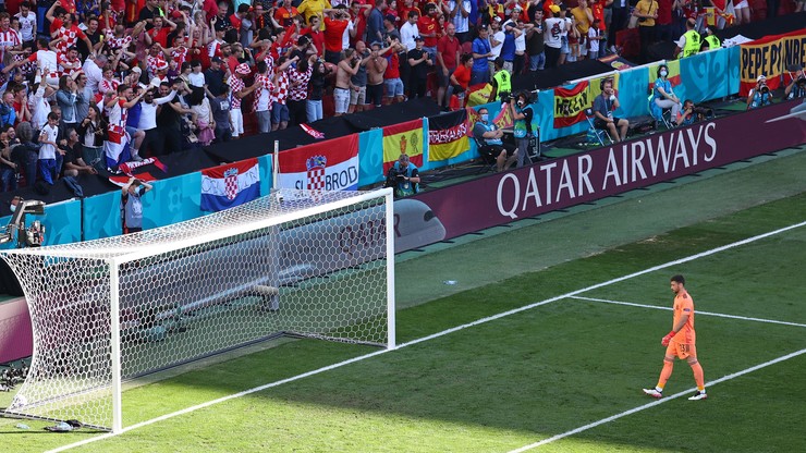 Bramkarz Unai Simon idzie w kierunku bramki, na trybunach widać kibic&oacute;w z flagami Chorwacji i Hiszpanii.