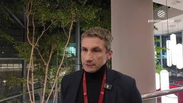 Remigiusz Rzepka, mężczyzna w czarnym golfie i marynarce, udziela wywiadu.