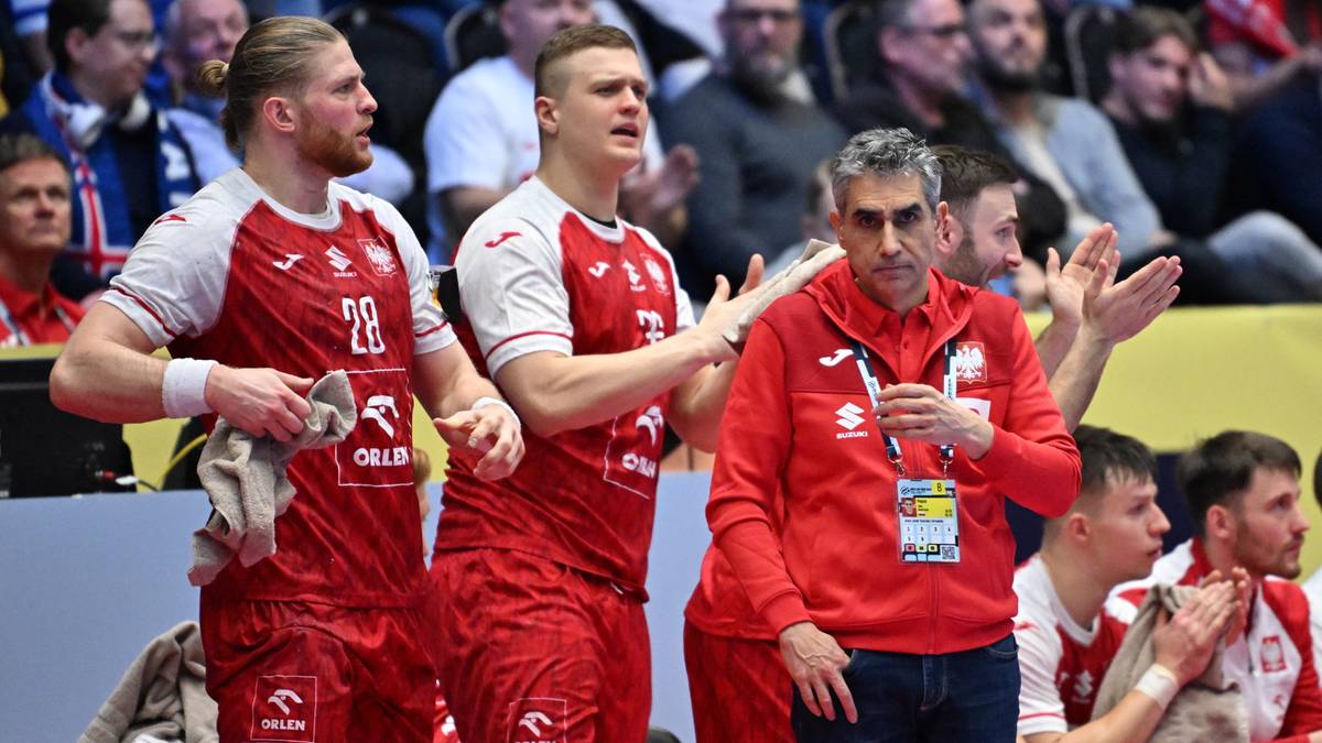 Drużyna piłkarzy ręcznych w czerwonych strojach, jeden z zawodnik&oacute;w trzyma ręcznik, na drugim planie widoczni kibice.