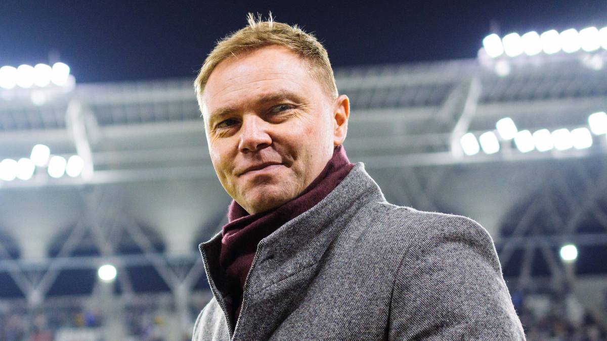 Mężczyzna w zimowym płaszczu na tle stadionu piłkarskiego przed meczem.