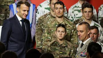 Prezydent Francji Emmanuel Macron stoi po lewej stronie, patrząc w kierunku grupy żołnierzy w mundurach.