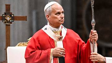 Papież ubrany w czerwone szaty liturgiczne i białą mitrę trzyma pastorał podczas ceremonii w kościele.
