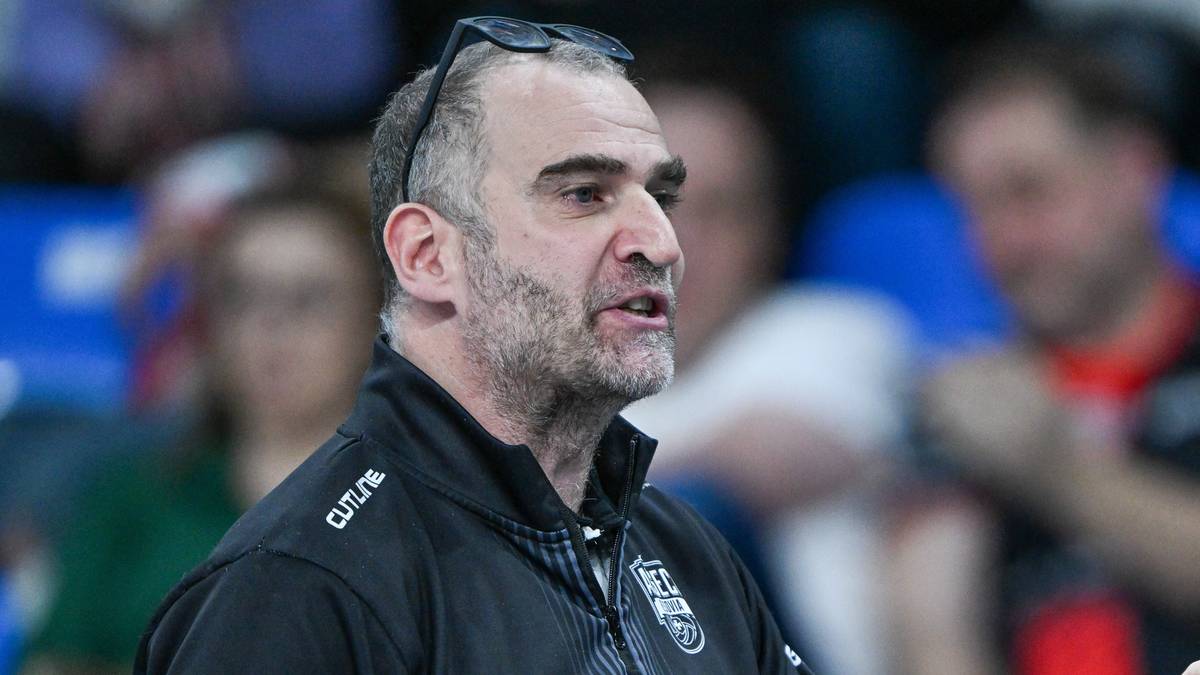 Trener drużyny siatkarskiej gestykuluje podczas meczu, trzymając w ręku kartkę z notatkami.