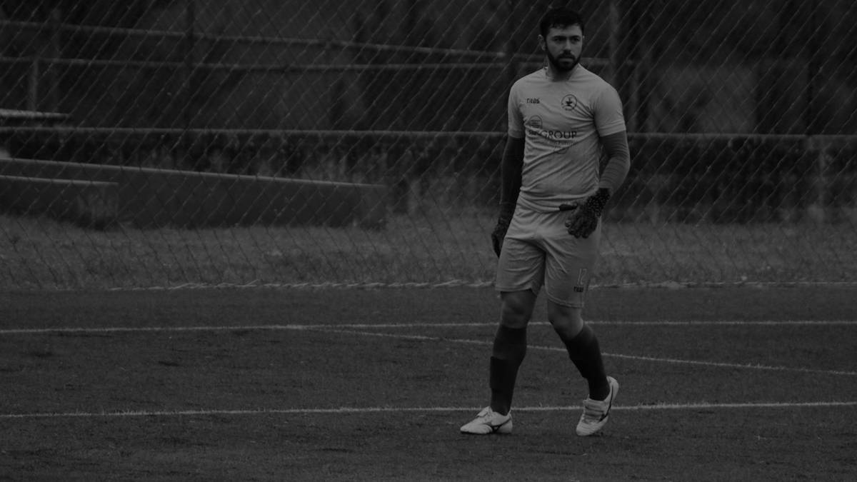 Młody mężczyzna w stroju piłkarskim, lekko pochylony, idzie po boisku.