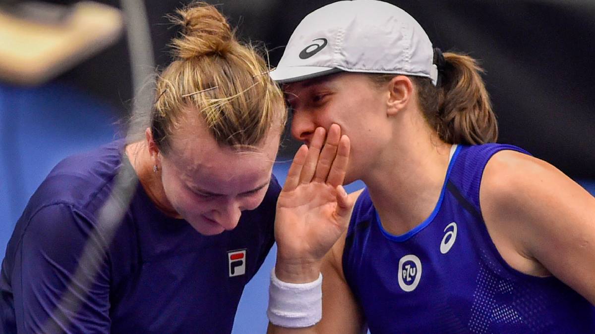 Dwie tenisistki w strojach sportowych, jedna szepcze drugiej do ucha.