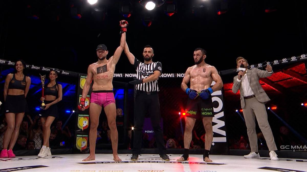 Dw&oacute;ch zawodnik&oacute;w MMA na ringu, jeden z uniesioną ręką triumfalnie