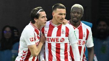 Trzech piłkarzy FC Koeln w czerwono-białych pasiaste strojach świętuje gola na boisku.