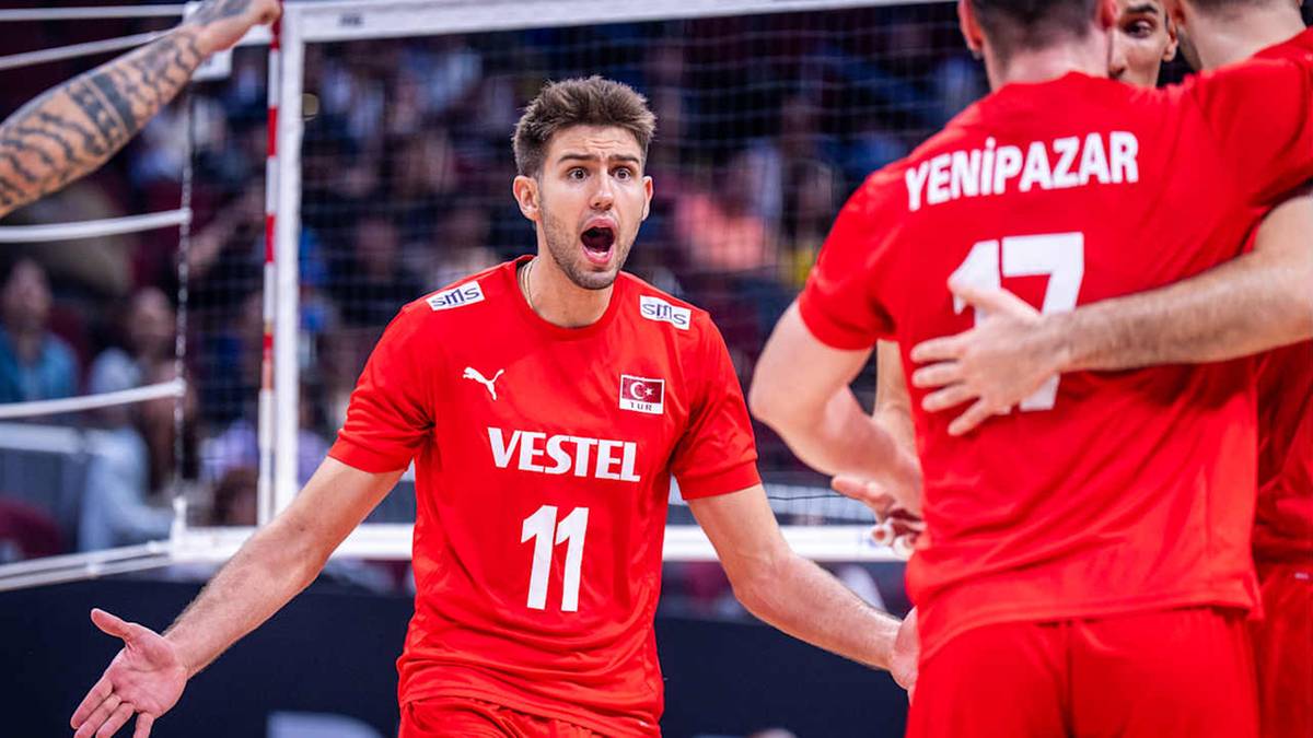 Siatkarz w czerwonej koszulce z numerem 11 i napisem "VESTEL" krzyczy z otwartymi ustami i szeroko otwartymi ramionami, podczas gdy inni gracze w czerwonych koszulkach zbliżają się do niego.