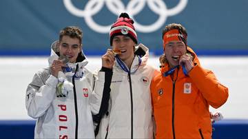 Trzech zawodnik&oacute;w na podium olimpijskim, dw&oacute;ch z nich trzyma medale. Na środku zawodnik z złotym medalem, po jego lewej zawodnik ze srebrnym medalem.