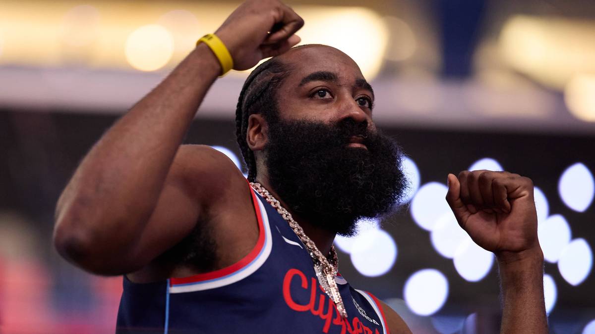 James Harden, koszykarz, w niebieskim stroju sportowym, z uniesioną ręką i zaciśniętą pięścią, z charakterystyczną brodą i złotym łańcuchem na szyi.