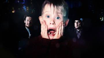 Zbliżenie na twarz chłopca z szeroko otwartymi ustami i dłońmi przy policzkach, otoczonego przez dw&oacute;ch mężczyzn.