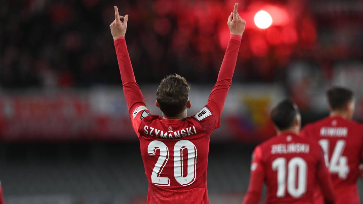 Piłkarz w czerwonej koszulce z numerem 20 świętuje strzelenie bramki, unosząc ręce w geście triumfu.