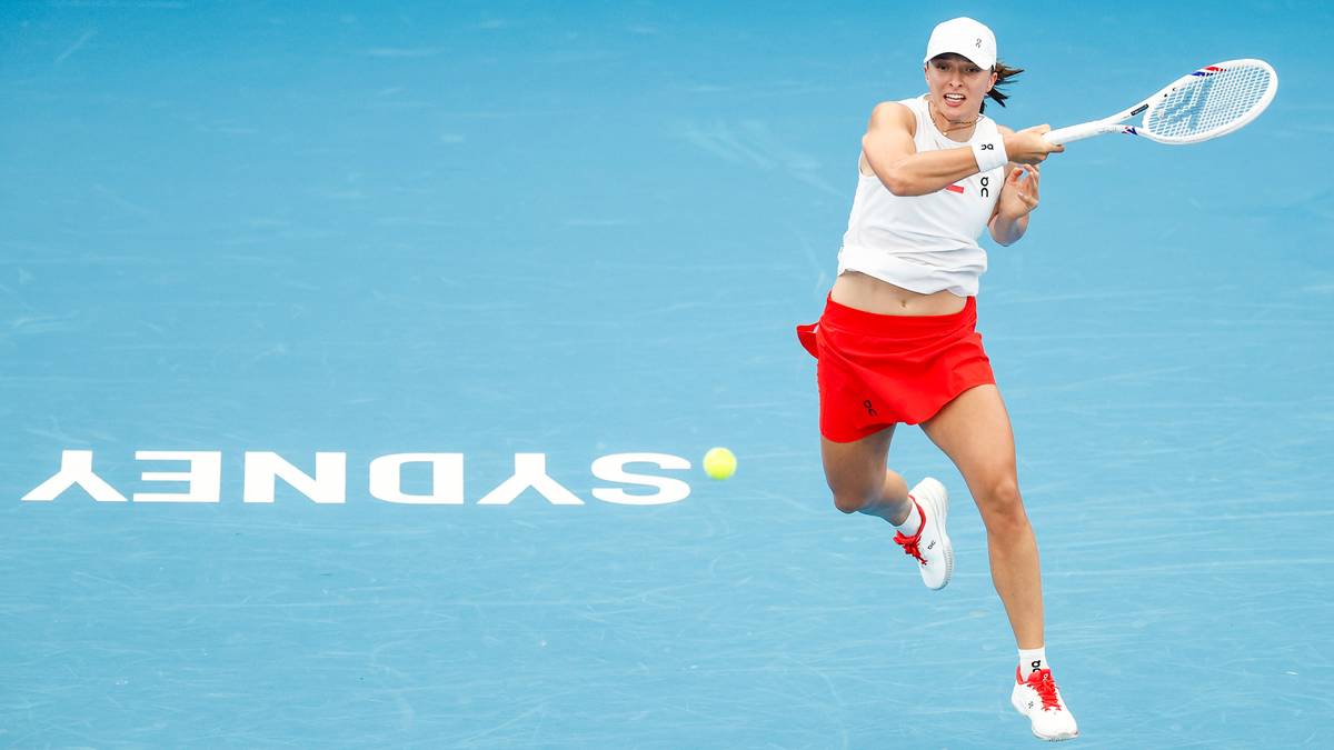 Iga Świątek uderza piłkę tenisową na niebieskim korcie z napisem "SYDNEY" w tle.