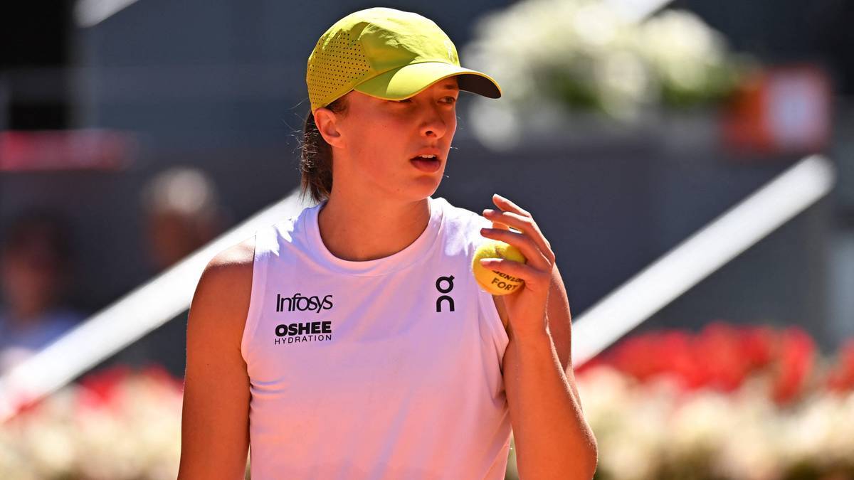 Iga Świątek, zawodniczka tenisa, w białej koszulce bez rękawów i żółtej czapce z daszkiem, trzymająca w dłoni piłkę tenisową.