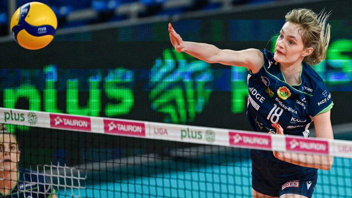 Siatkarka w niebieskim stroju z numerem 18 na plecach wykonuje zagrywkę podczas meczu siatkówki.