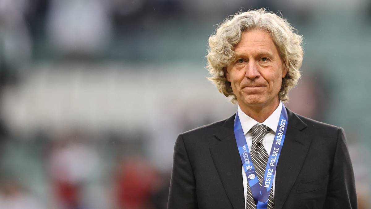 Starszy mężczyzna w garniturze i krawacie, z kręconymi siwymi włosami.