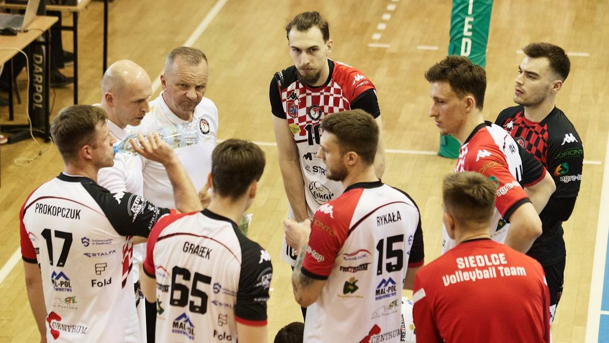 Drużyna siatkarska KPS Siedlce w trakcie zbiórki taktycznej, otaczając swojego trenera.