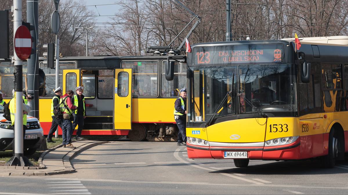 Autobus i tramwaj komunikacji miejskiej stojące na drodze, obok nich pracownicy służb w kamizelkach odblaskowych.
