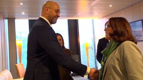 Mężczyzna i kobieta ściskają sobie dłonie wewnątrz pomieszczenia, prawdopodobnie podczas spotkania delegacji.