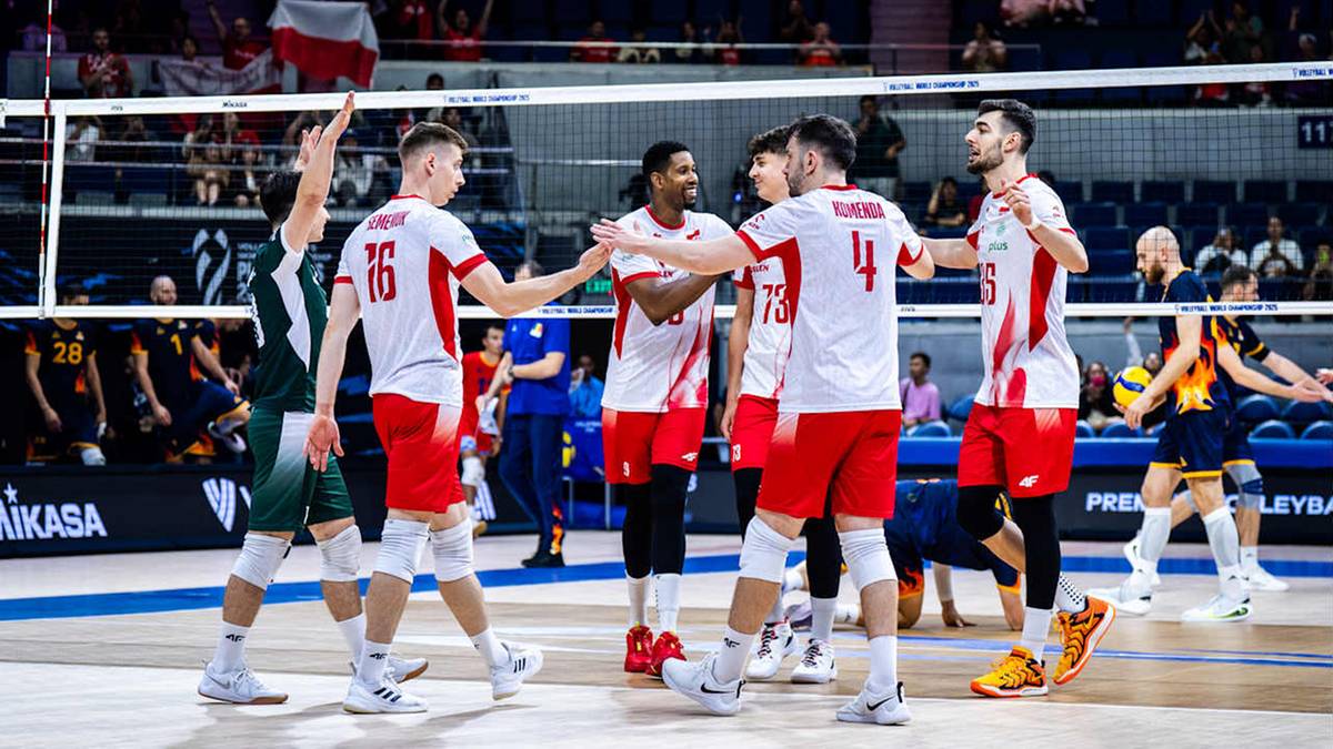 Drużyna siatkarzy w czerwonych strojach świętuje na boisku z siatką w tle.