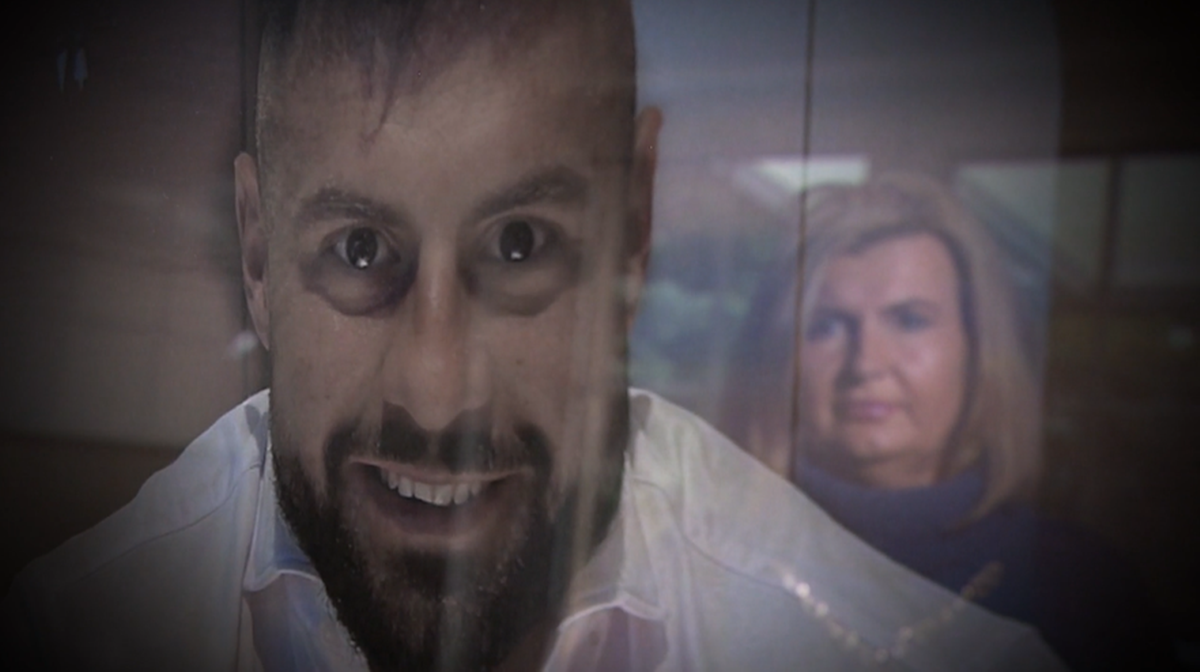 Zbliżenie na twarz mężczyzny z szeroko otwartymi oczami i lekko uchylonymi ustami, sugerującymi zaskoczenie lub przerażenie. W tle, za nim, widoczna jest twarz kobiety.