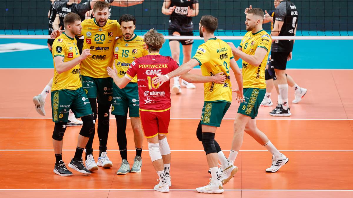 Drużyna siatkarzy w ż&oacute;łto-zielonych strojach świętuje na boisku, jeden zawodnik w czerwonej koszulce stoi pośrodku.