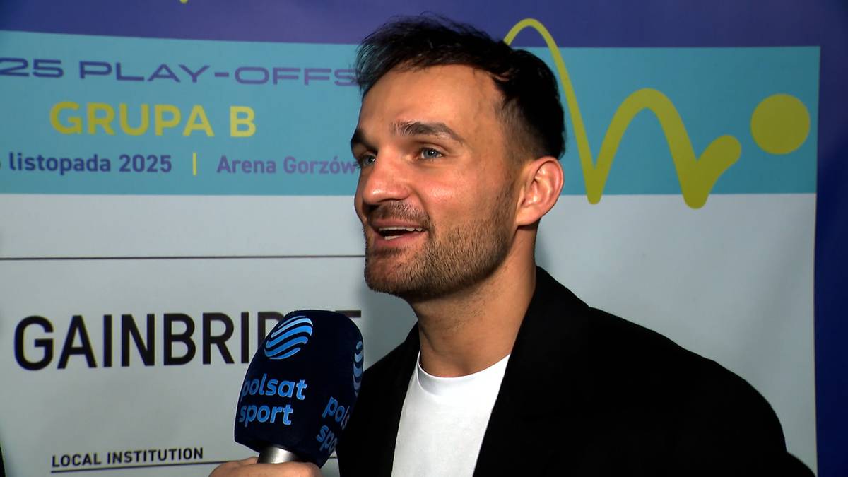 Portret Bartosza Zmarzlika podczas wywiadu. Uśmiechnięty mężczyzna z krótkimi włosami i zarostem, ubrany w białą koszulkę i czarną marynarkę, trzyma mikrofon Polsat Sport.