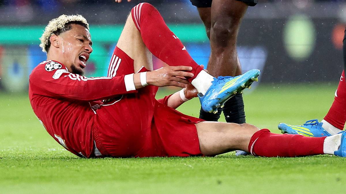 Piłkarz Liverpoolu leży na boisku, trzymając się za nogę i wykrzywiając się z b&oacute;lu.