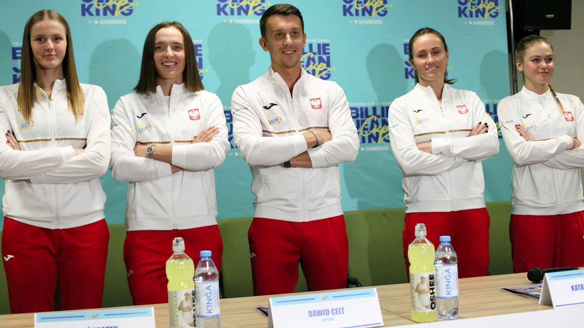 Pięć osób w strojach sportowych z logo Billie Jean King Cup, stojących z założonymi rękami.