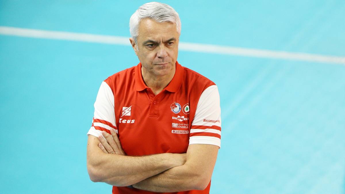 Mężczyzna w czerwono-białej koszulce polo z rękami skrzyżowanymi na piersi.