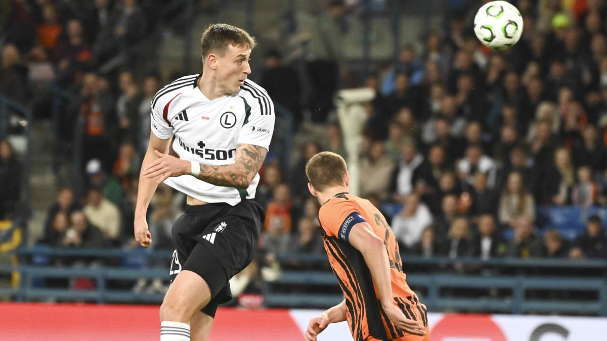 Piłkarz Legii Warszawa w białej koszulce z numerem 5 z czarnymi spodenkami i białymi skarpetkami wykonuje główkę.