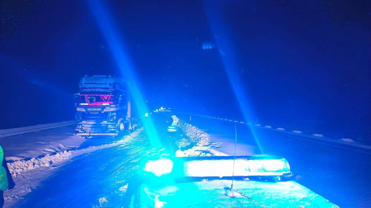 Śnieg na drodze, światła policyjne, ciężar&oacute;wka w oddali.