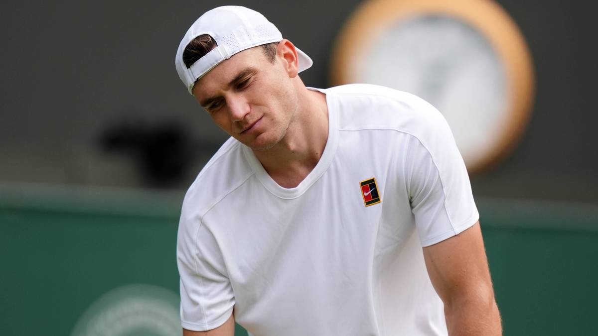 Tenisista w białej czapce i koszulce, pochylający głowę w wyrazie smutku lub bólu.