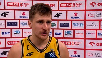 Portret Jakuba Schenka, koszykarza w ż&oacute;łtej koszulce, podczas wywiadu na tle ścianki sponsorskiej.