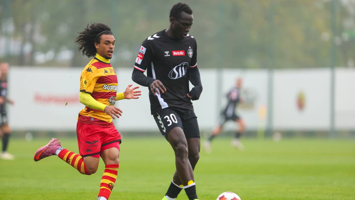 Dw&oacute;ch piłkarzy podczas meczu piłki nożnej, jeden w czarnej koszulce z numerem 30, drugi w ż&oacute;łto-czerwonym stroju.