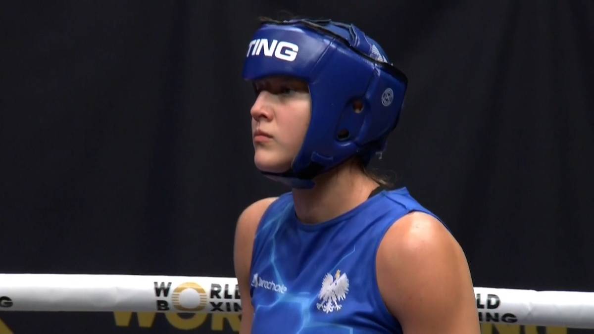 Bokserka w niebieskim kasku i stroju sportowym patrzy w bok.