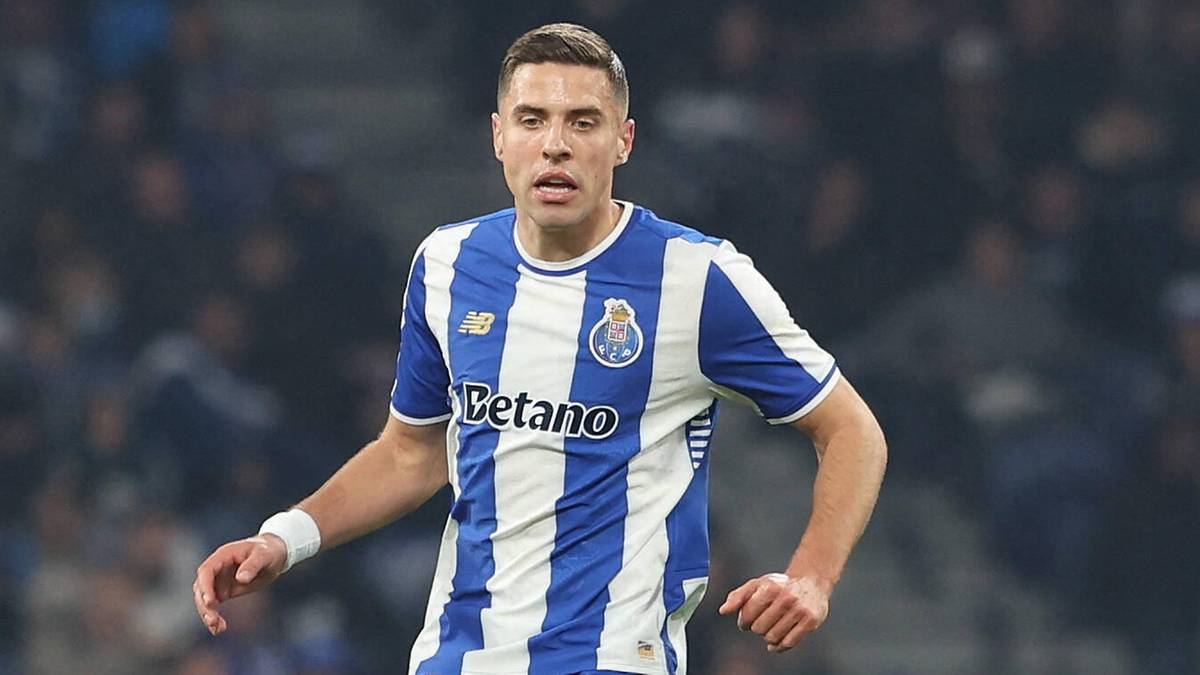 Piłkarz w niebiesko-białym stroju FC Porto biegnie z piłką na boisku, z drugim zawodnikiem w ż&oacute;łtym stroju na pierwszym planie.