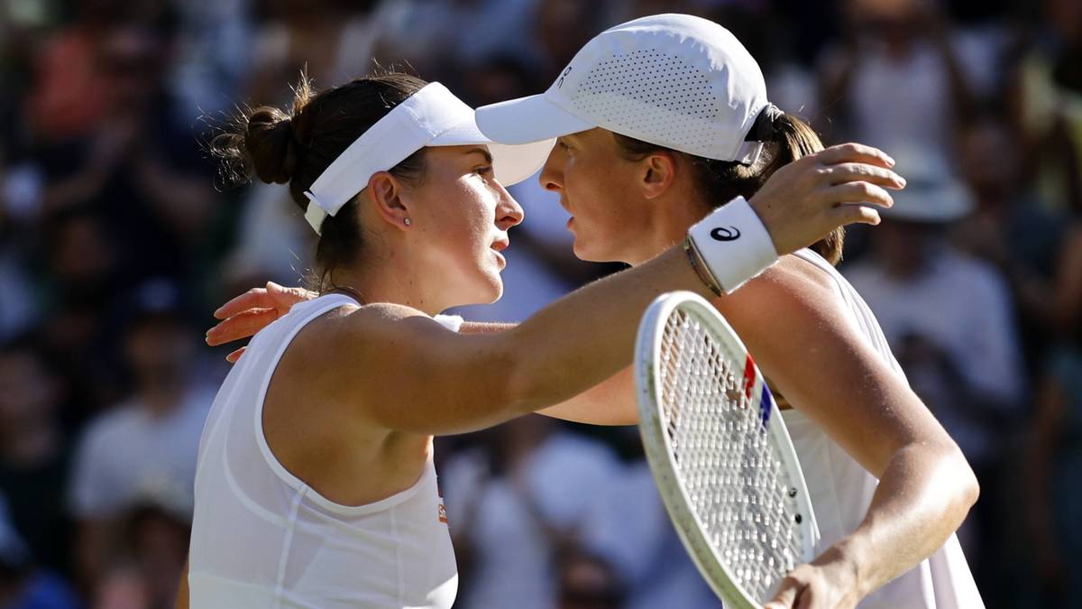 Dwie tenisistki w białych strojach sportowych i czapkach z daszkiem przytulają się po meczu na Wimbledonie. Jedna z nich trzyma rakietę tenisową.