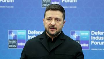 Wołodymyr Zełenski, prezydent Ukrainy, gestykuluje podczas przem&oacute;wienia na tle niebieskiej ściany z logo NATO i "Defence Industry Forum".