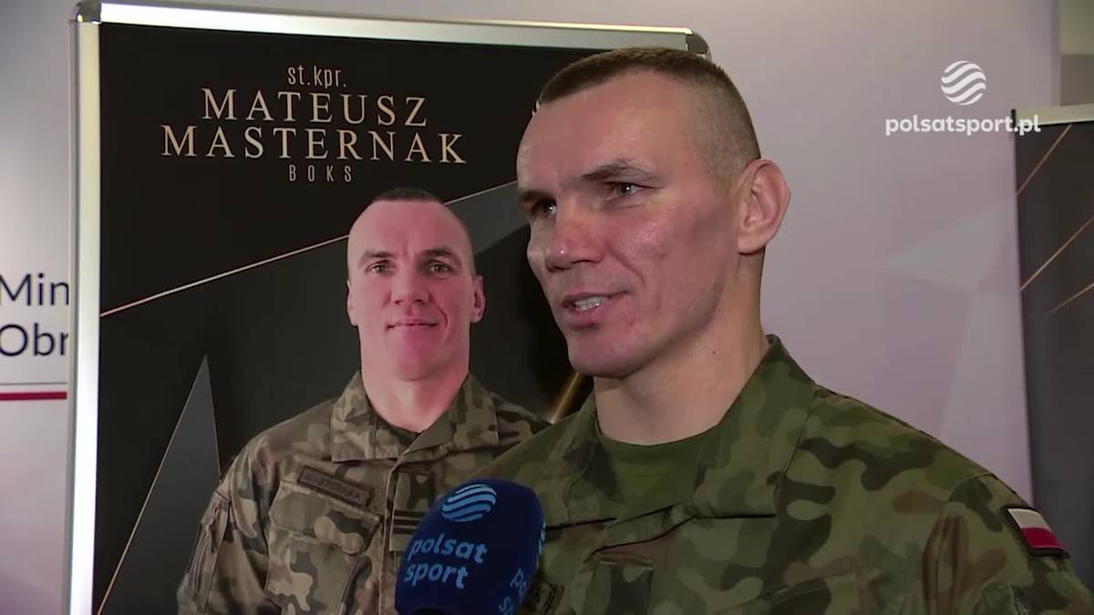 Mateusz Masternak w mundurze wojskowym udziela wywiadu, w tle plakat z jego wizerunkiem.