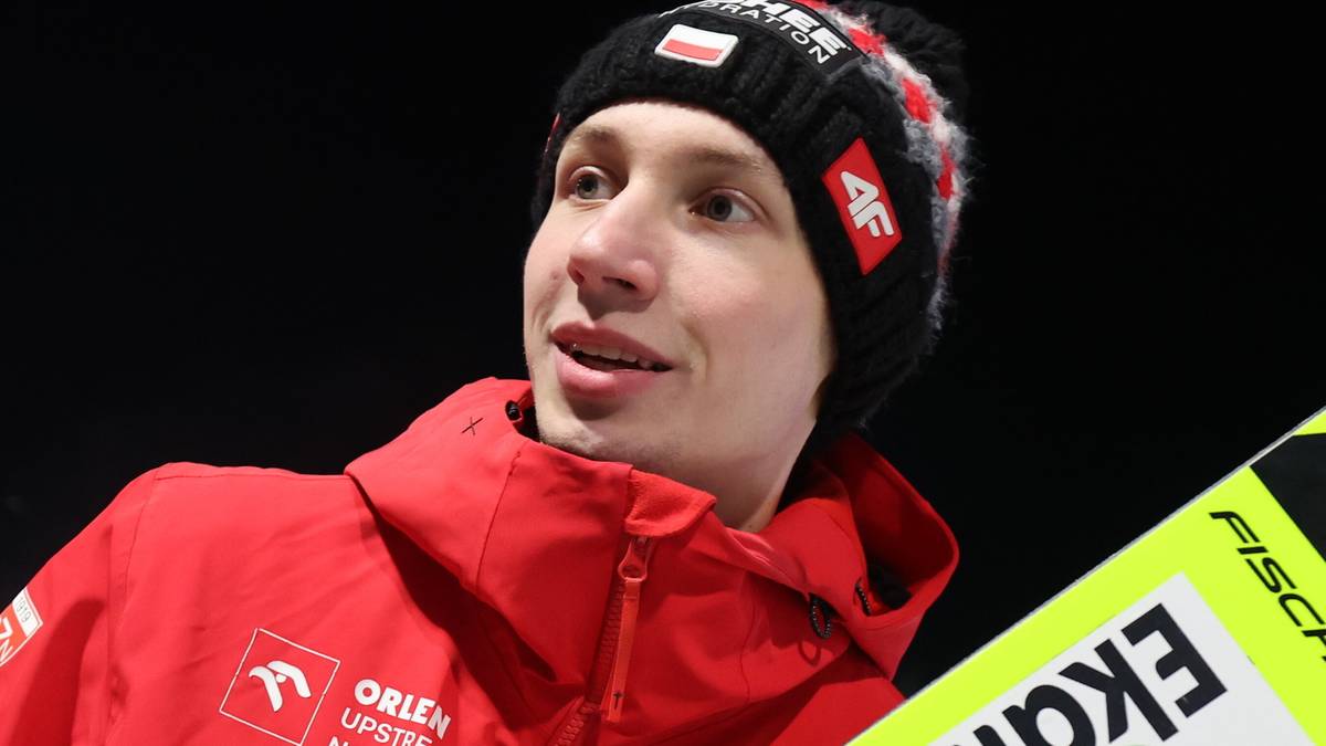 Skoczek narciarski w czerwonym stroju trzymający nartę.